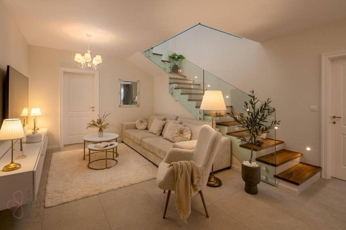 Elegantes Wohnzimmer mit bequemer Couch, stilvoller Einrichtung und einer modernen Treppe mit Glasgeländer.