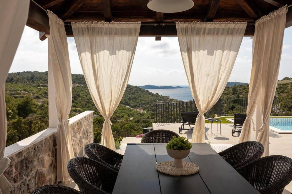 Heller Pavillon mit Esstisch und Meerblick, umgeben von grüner Landschaft, ideal für Mahlzeiten im Freien.