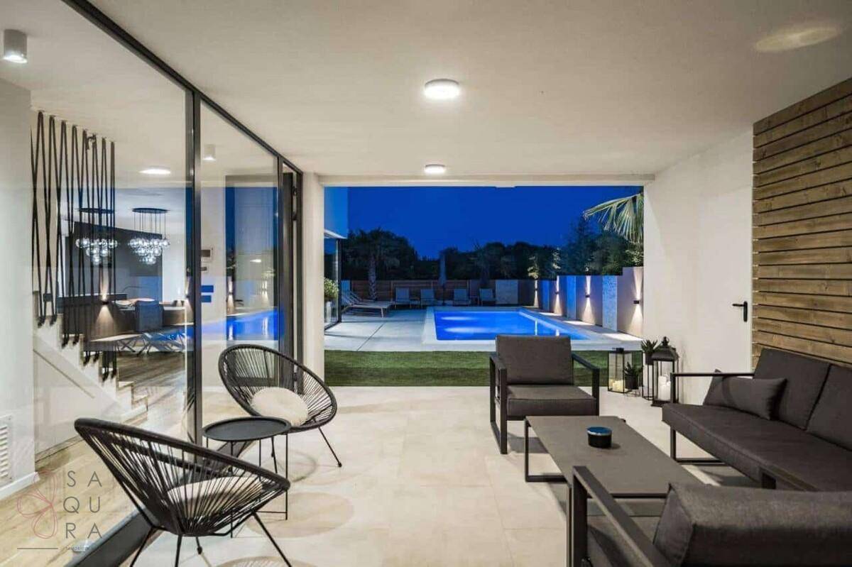 Überdachte Terrasse mit modernen Lounge-Möbeln und Blick auf den beleuchteten Poolbereich.