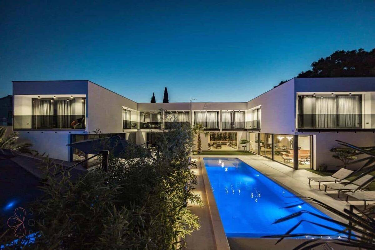 Beeindruckende moderne Villa bei Nacht mit leuchtendem Pool und eleganter Architektur.