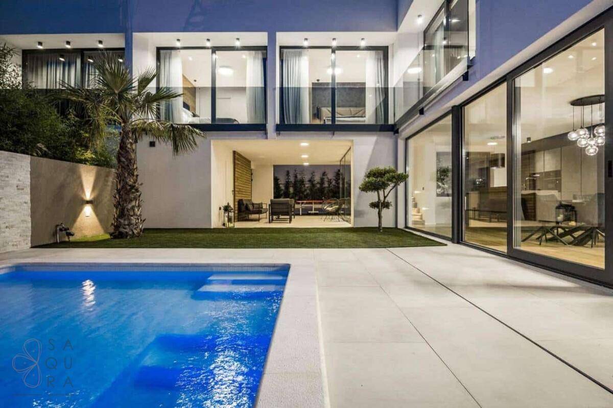 Elegante Villa mit beleuchtetem Pool und weitläufigen Terrassenbereichen bei Nacht.
