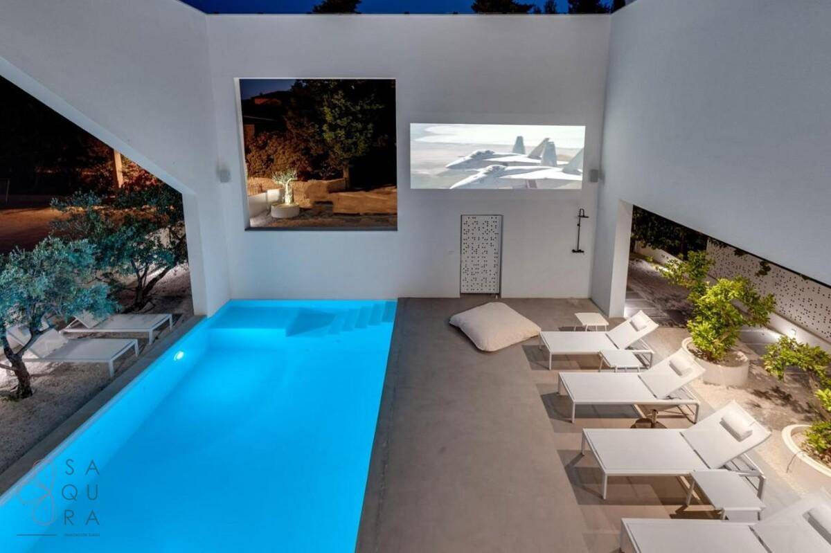 Beleuchteter Poolbereich bei Nacht mit Liegestühlen und Projektion an der Wand.