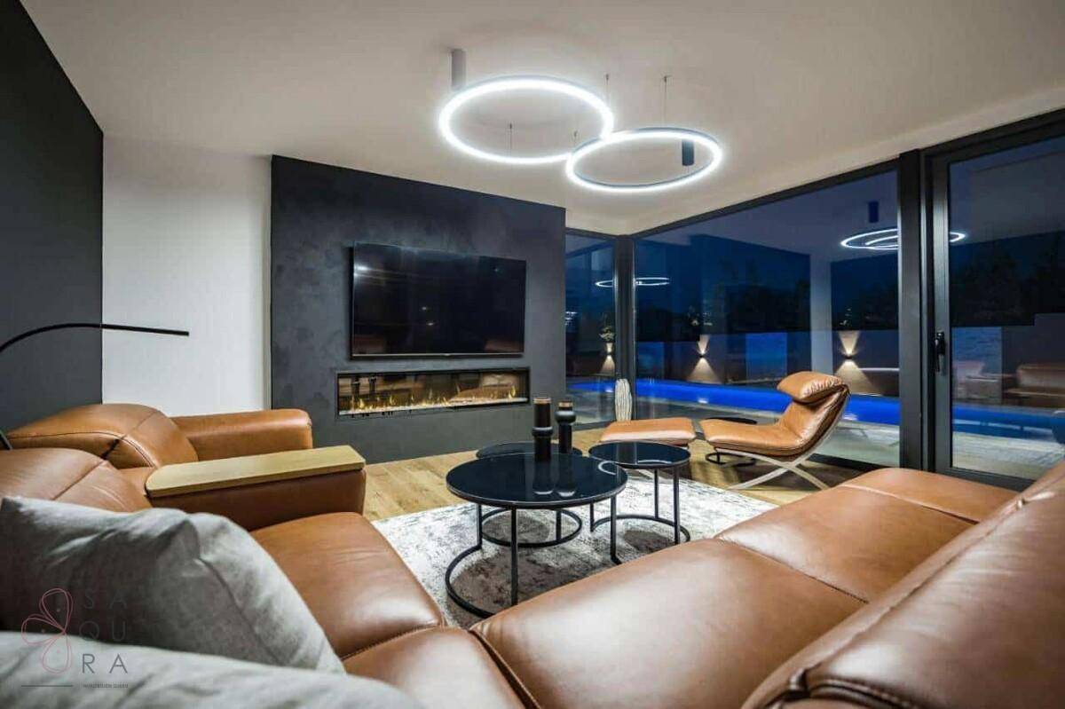 Modernes Wohnzimmer mit bequemen Ledersofas, Kamin und Blick auf den beleuchteten Pool.