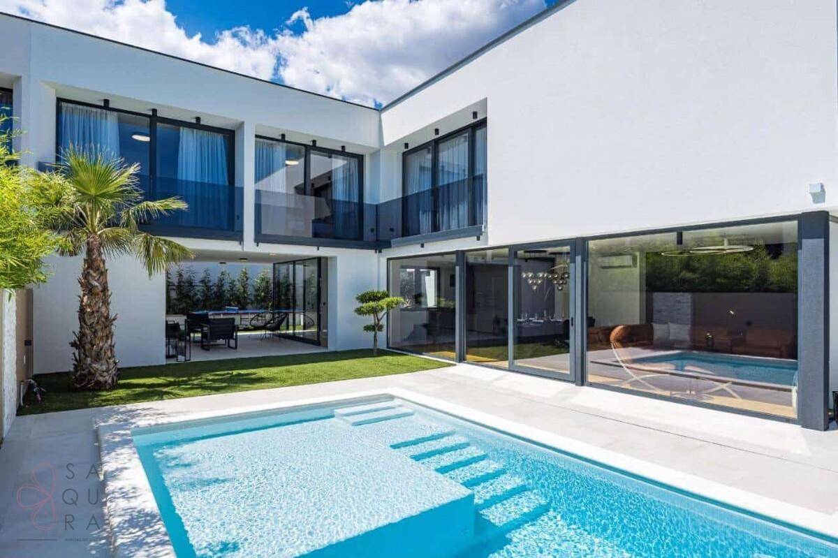 Heller Poolbereich mit Stufen und Blick auf die großzügigen Glasfronten der Villa.