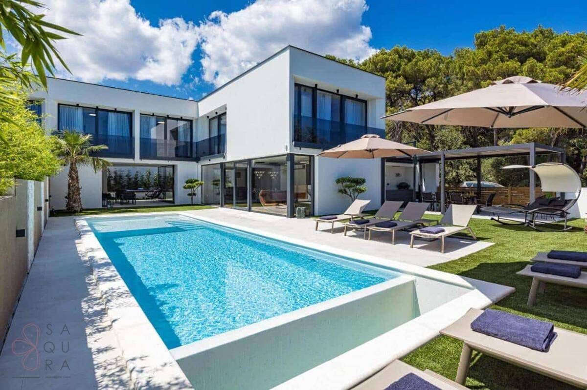 Sonniger Poolbereich mit Liegestühlen, Sonnenschirmen und der modernen Architektur der Villa.