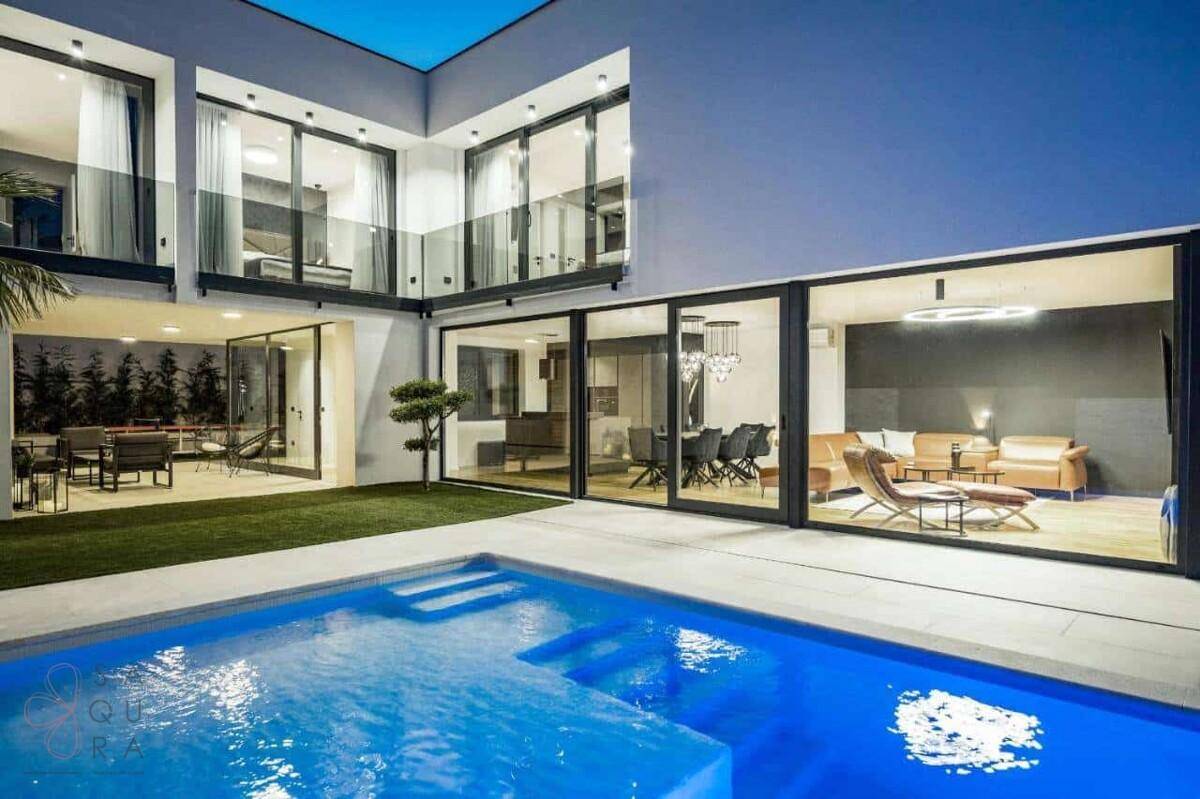Moderner Poolbereich mit Stufen und Blick auf die großzügigen Glasfronten der Villa.
