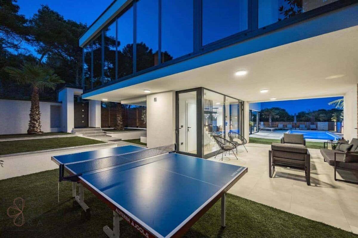 Überdachter Außenbereich mit Tischtennisplatte und Lounge-Möbeln neben der modernen Villa.