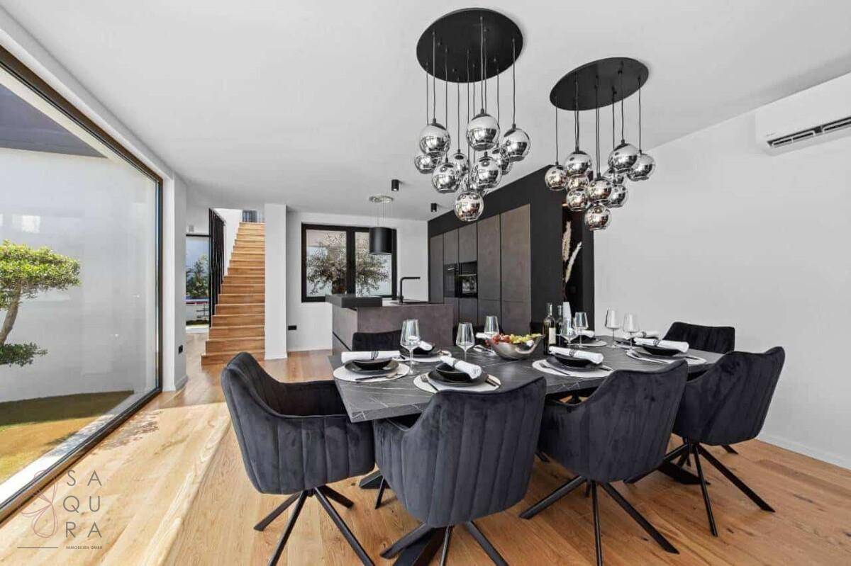 Moderner Essbereich mit großem Tisch, Designerleuchten und offener Küche im Hintergrund.