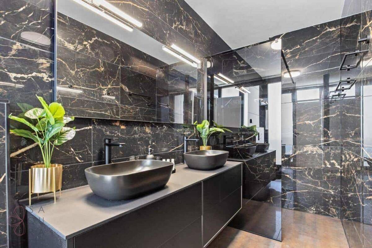Luxuriöses Badezimmer mit schwarzen Marmorfliesen, Doppelwaschbecken und modernen Armaturen.