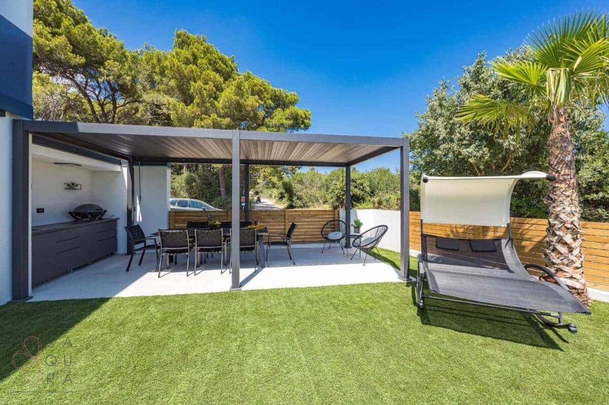Stilvolle überdachte Terrasse mit Außenküche, Essbereich und Sonnenliege im Garten.