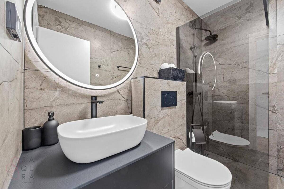 Helles Badezimmer mit modernen Fliesen, beleuchtetem Spiegel und begehbarer Dusche.