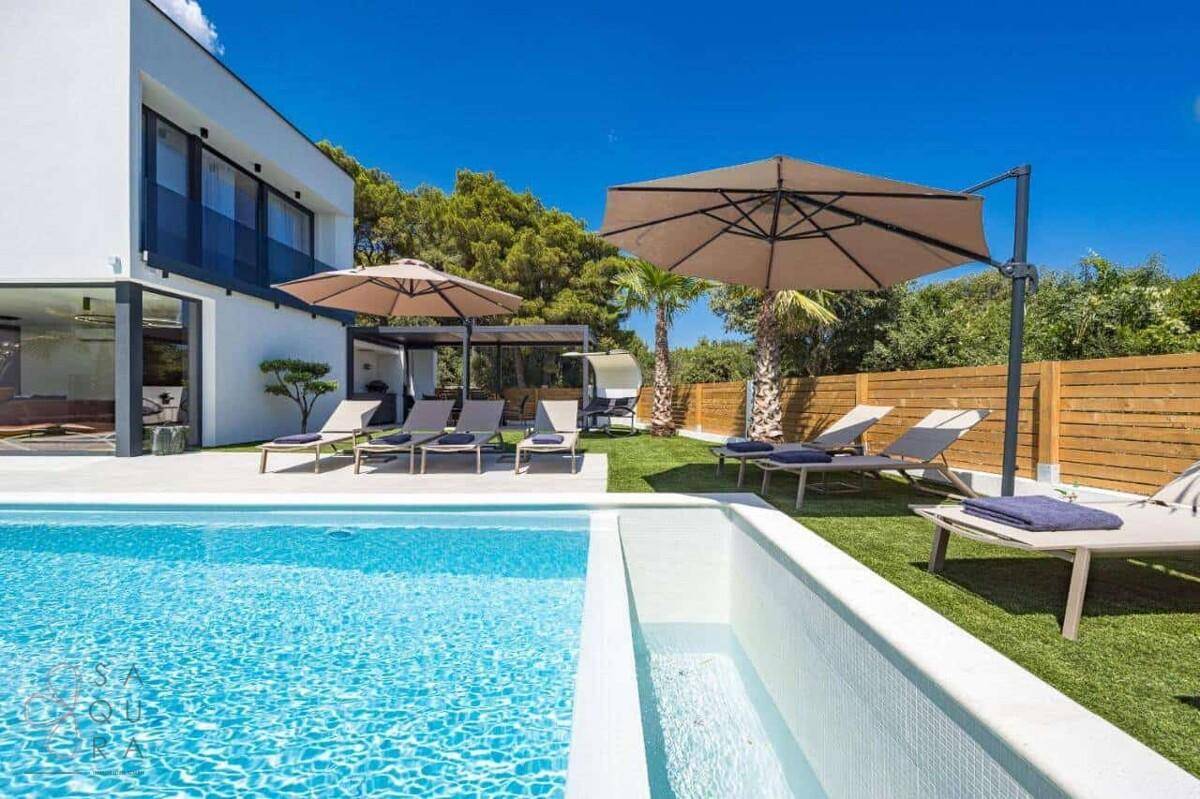 Entspannender Gartenbereich mit Liegestühlen, Sonnenschirmen und Blick auf den Pool.