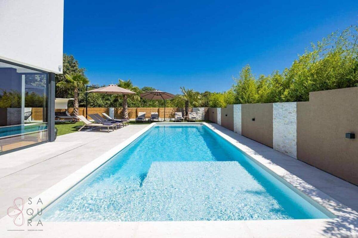 Erfrischender Pool mit integrierten Stufen, umgeben von einer sonnigen Terrasse und Grünflächen.