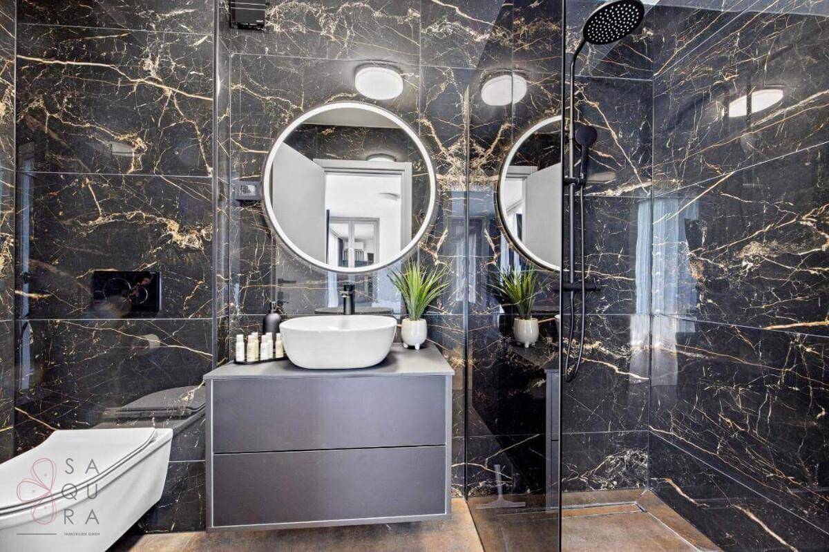 Modernes Badezimmer mit schwarzen Marmorfliesen, runden Spiegeln und begehbarer Dusche.