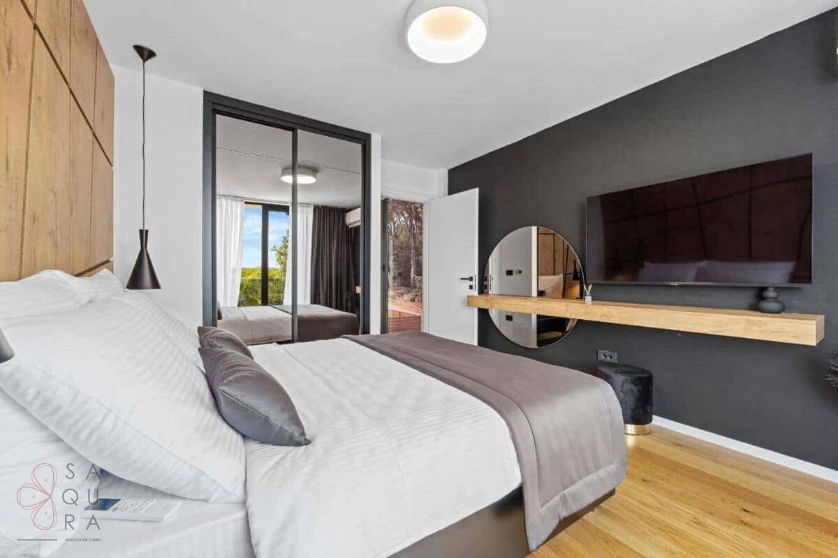 Modernes Schlafzimmer mit Holzbettkopfteil, Spiegelschränken und Fernseher.