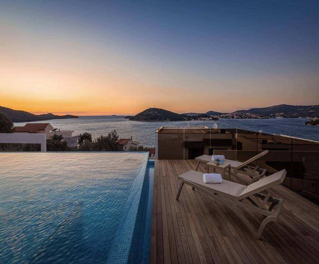 Infinity-Pool und Holzdeck bei Sonnenuntergang mit malerischem Meerblick.