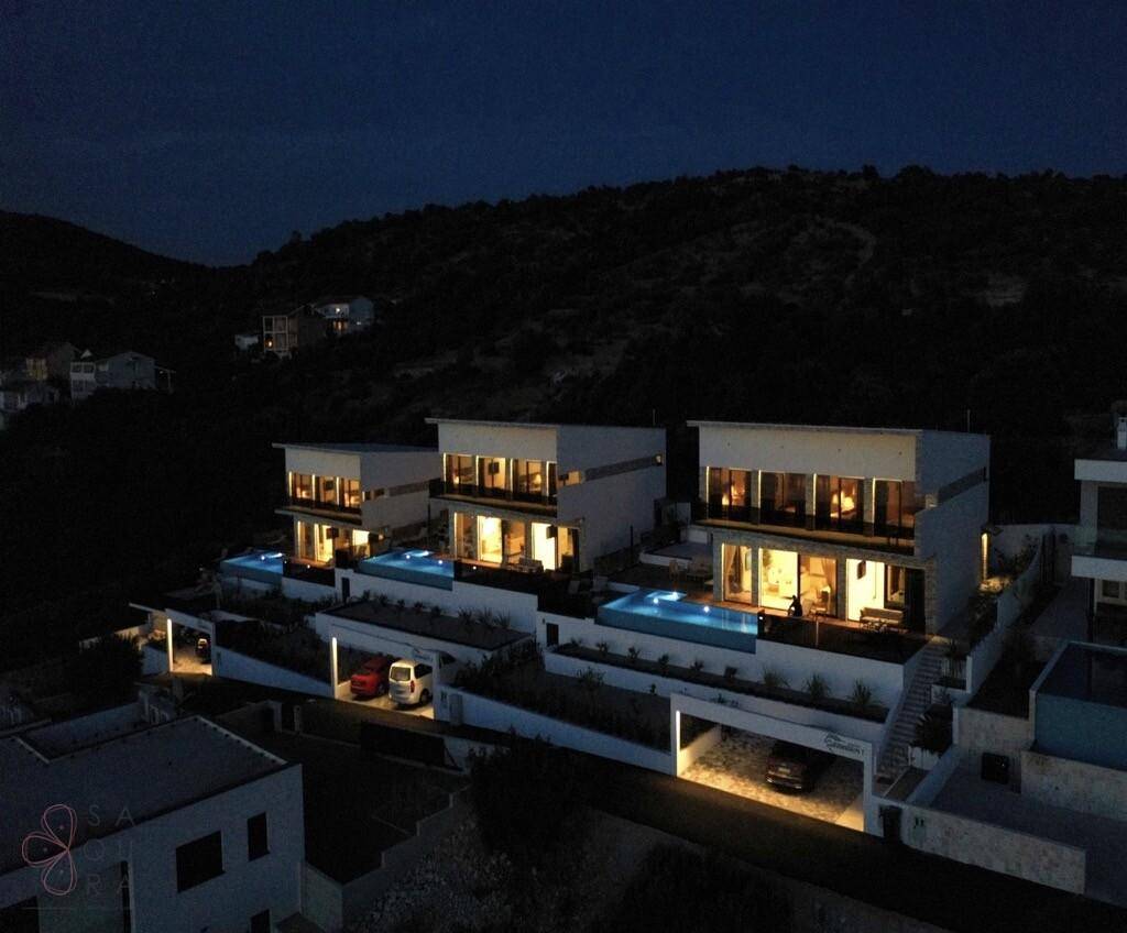 Reihe moderner Villen bei Nacht mit beleuchteten Pools und Terrassen.