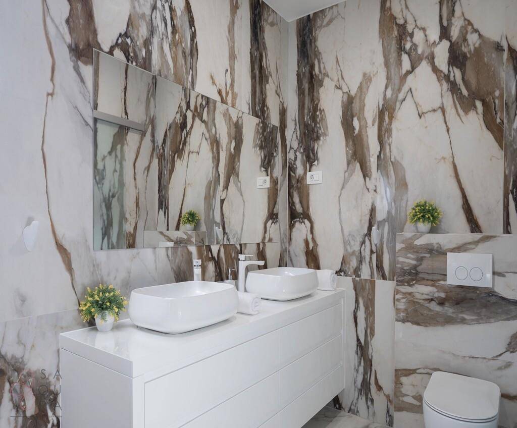 Luxuriöses Badezimmer mit Marmorwänden, Doppelwaschbecken und modernem Design.