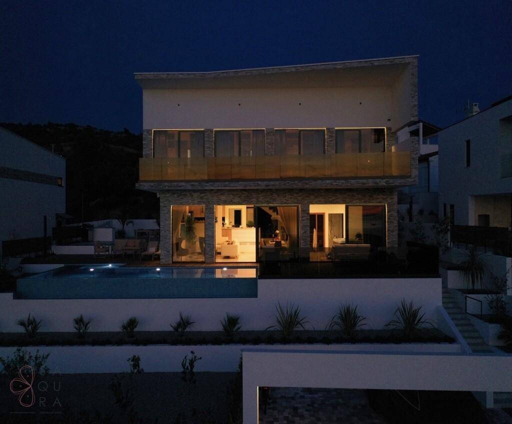 Elegante Villa bei Nacht mit beleuchteter Fassade und Poolbereich.