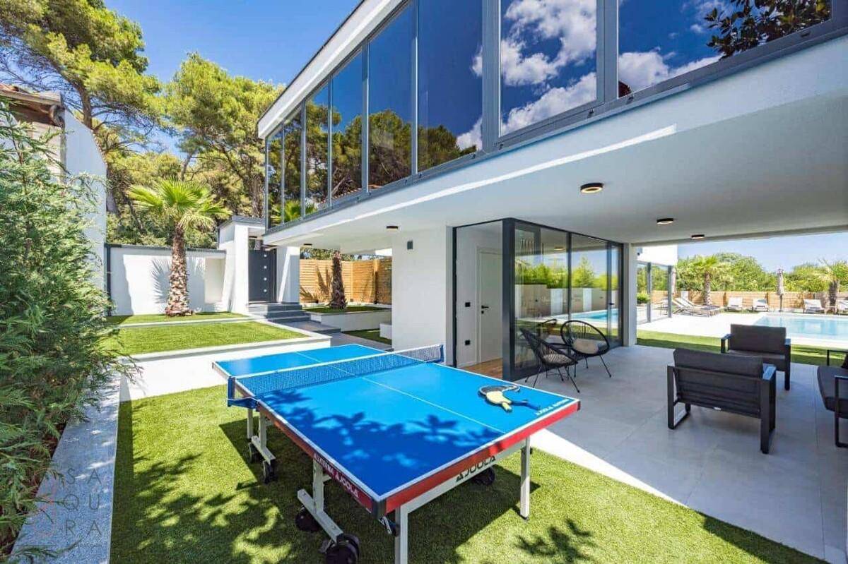 Außenbereich mit Tischtennisplatte und überdachter Lounge-Zone neben der modernen Villa.