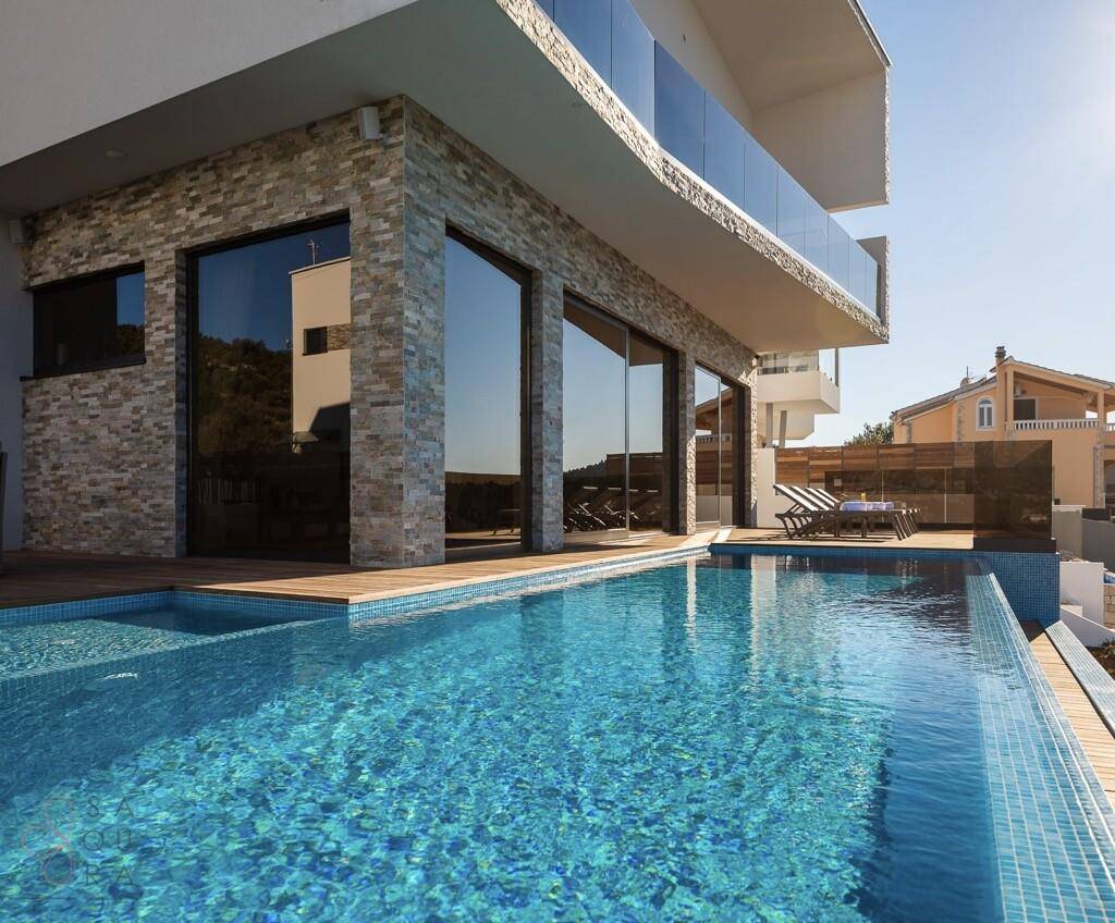 Moderne Villa mit Infinity-Pool und Holzdeck, umgeben von Steinmauern.