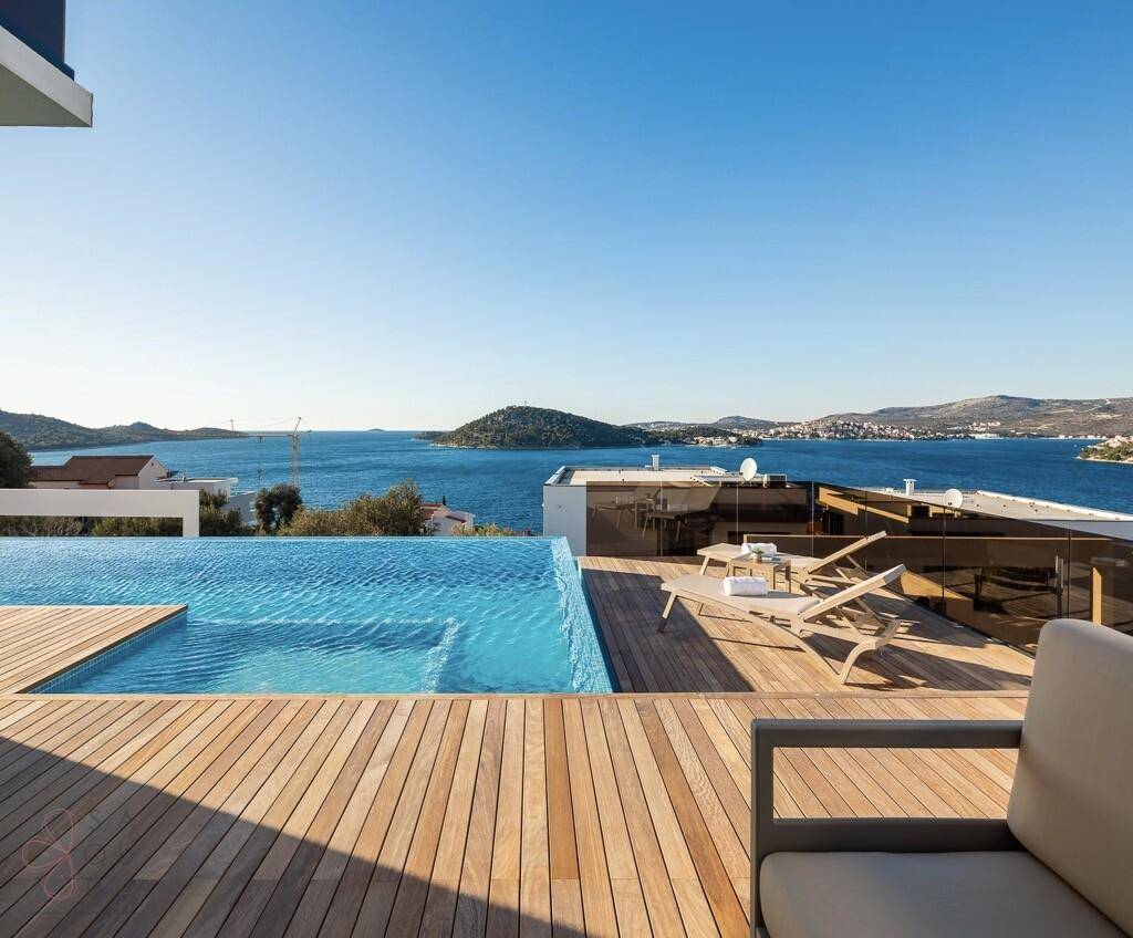 Geräumiges Holzdeck mit Sonnenliegen und Infinity-Pool mit weitem Meerblick.