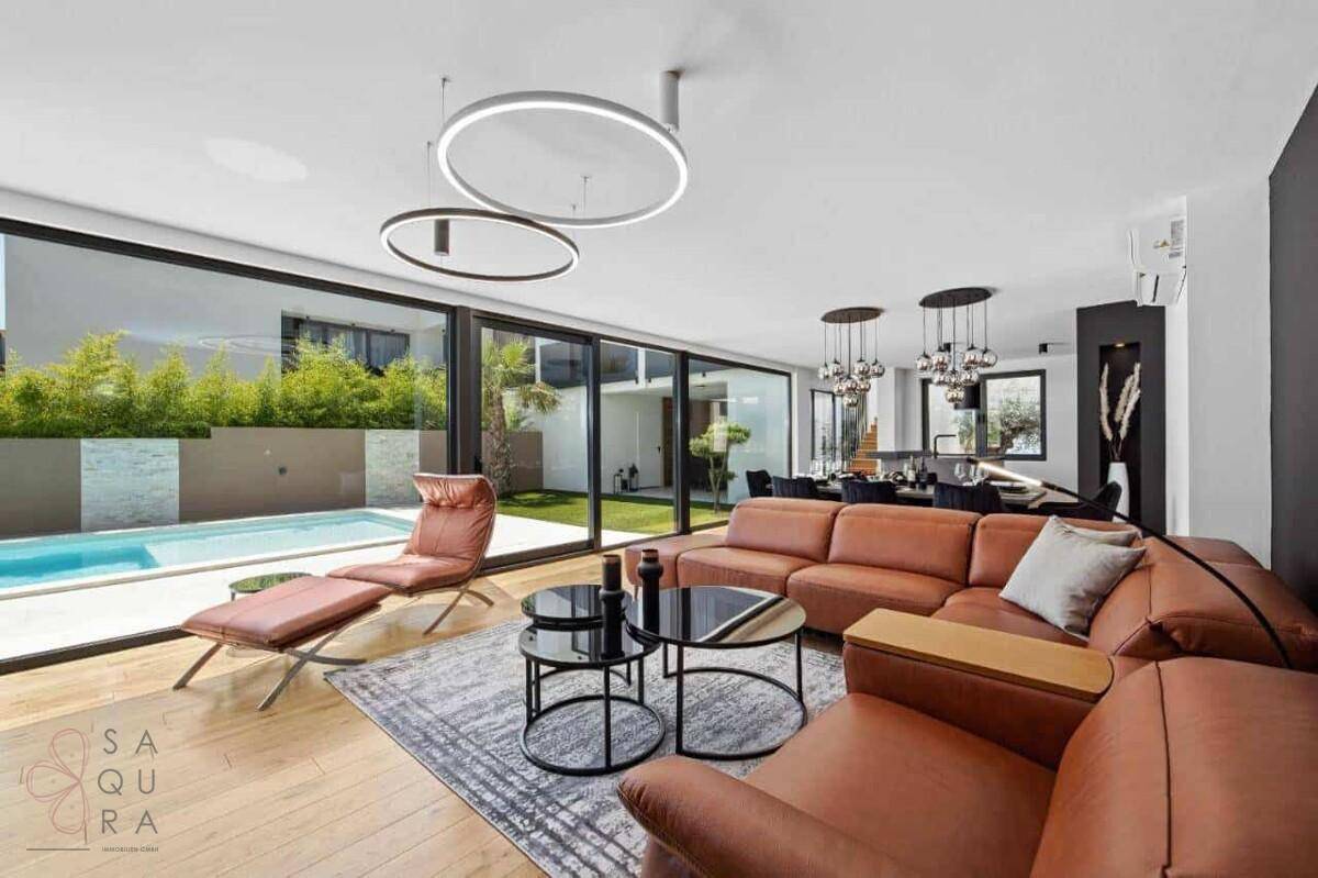 Offener Wohn- und Essbereich mit Ledersofas, modernen Leuchten und Blick auf den Pool.