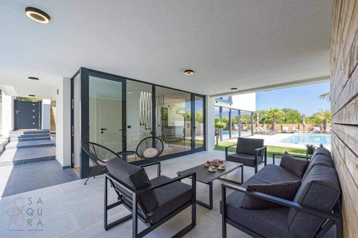Überdachte Terrasse mit modernen Lounge-Möbeln und Blick auf den sonnigen Poolbereich.