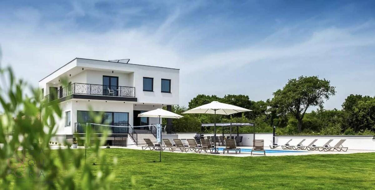 Weitläufiger Außenbereich einer modernen Villa mit Pool, Liegewiese und Volleyballnetz im Grünen.
