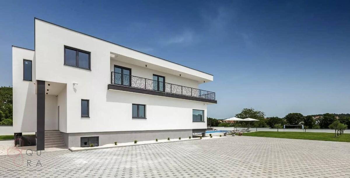 Moderne Villa mit großem gepflasterten Vorplatz und klaren architektonischen Formen.