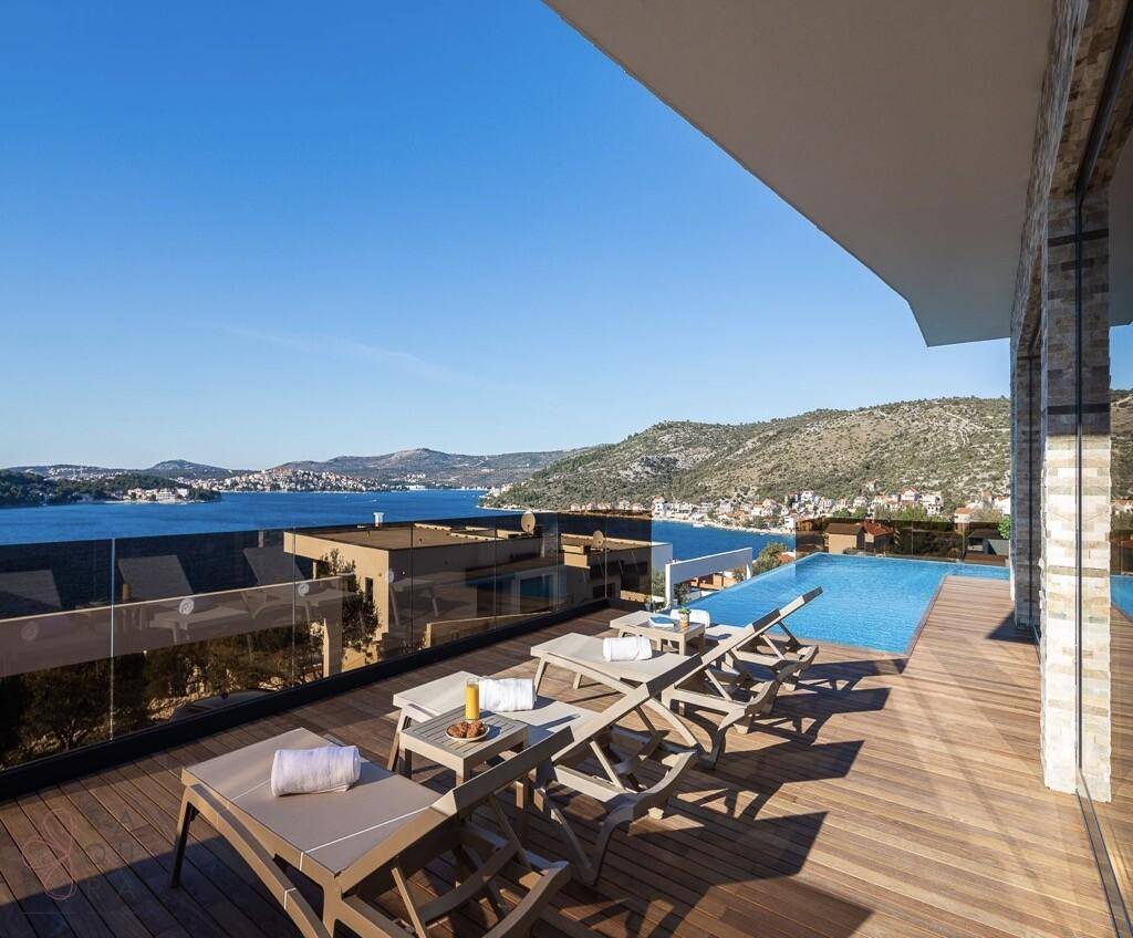 Großzügiges Holzdeck mit Sonnenliegen und Infinity-Pool mit weitem Meerblick.