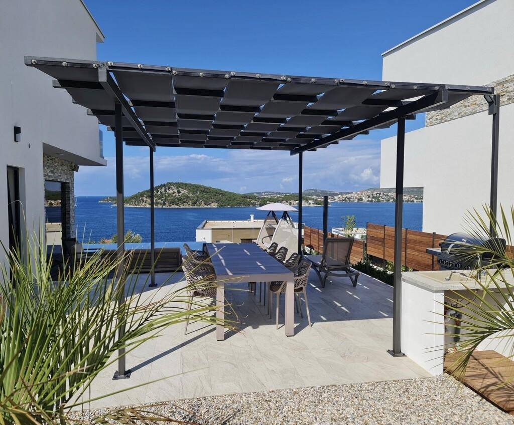 Überdachter Essbereich im Freien unter einer Pergola mit Grill und Meerblick.