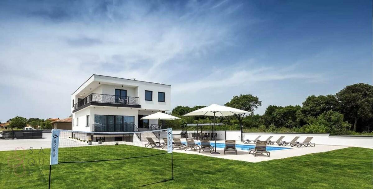 Weitläufiger Außenbereich der Villa mit Pool, Rasenfläche und Volleyballnetz für Freizeitaktivitäten.