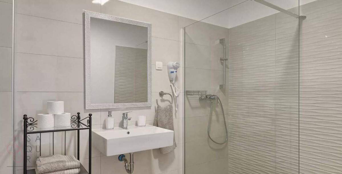 Helles Badezimmer mit moderner Dusche, Einzelwaschbecken und Spiegel.