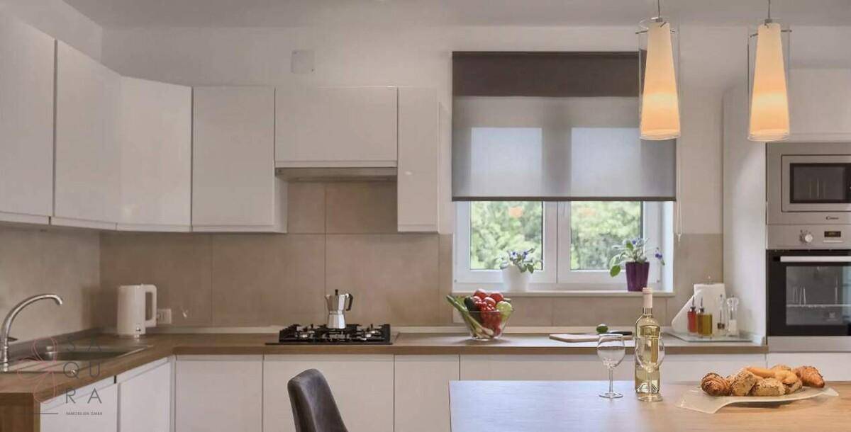 Moderne Einbauküche mit weißen Schränken, Holztheke und Blick ins Grüne.