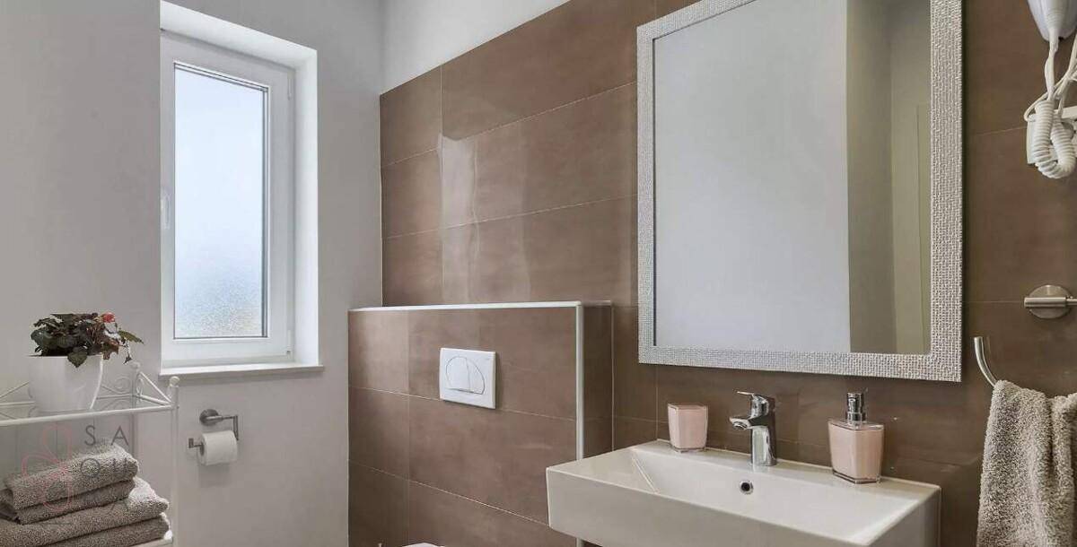Modernes WC mit wandhängender Toilette, Einzelwaschbecken und Fenster.