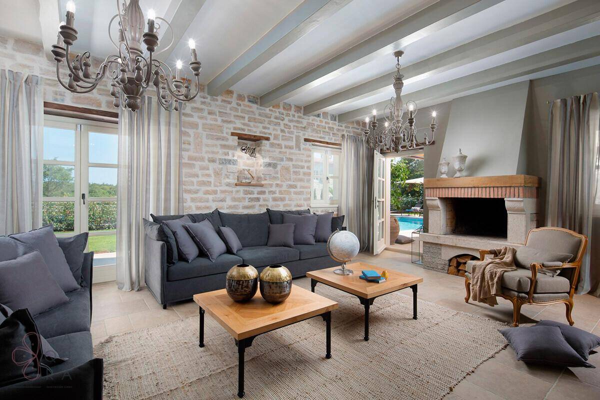 Geräumiges Wohnzimmer mit Steinwand, Kamin, Holzbalkendecke und Zugang zum Poolbereich.