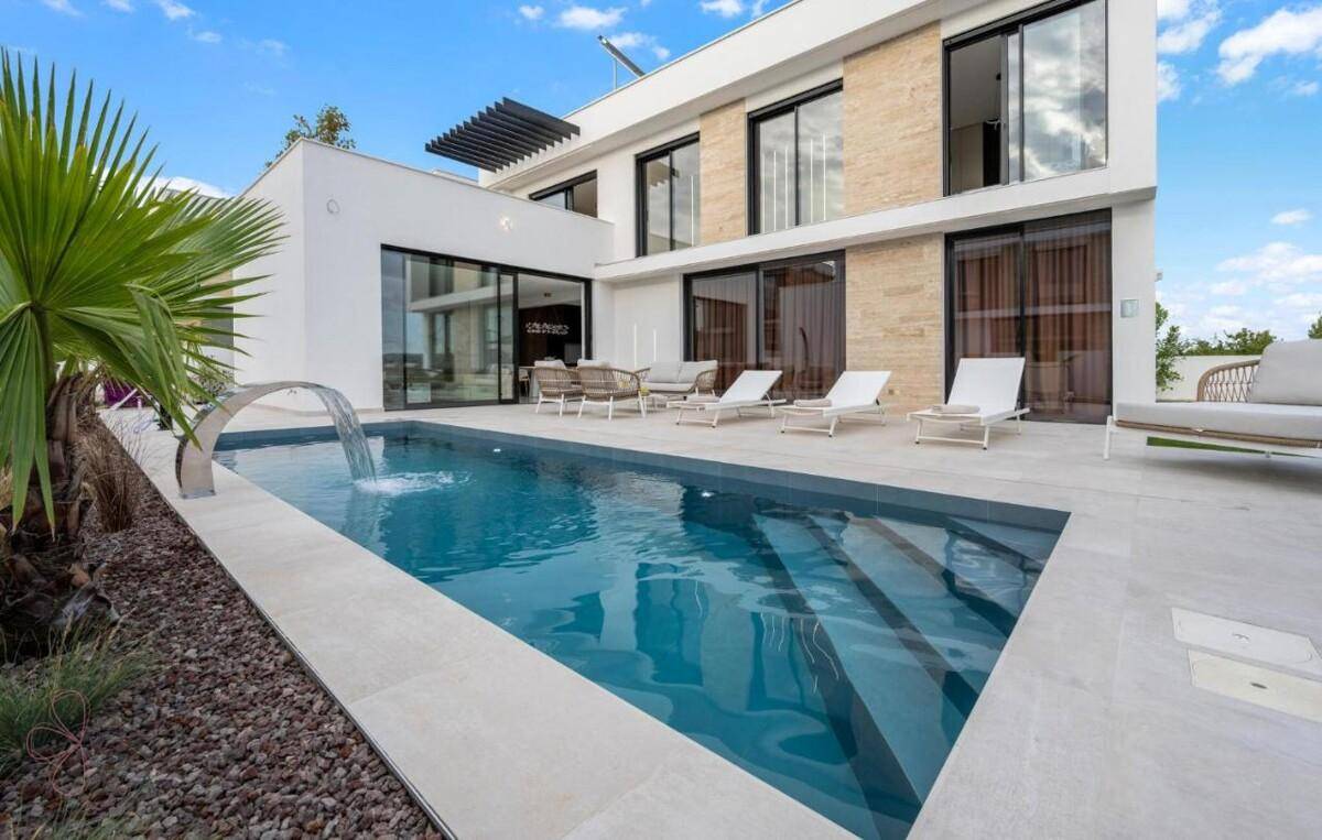 Moderner Poolbereich mit Wasserspiel, Liegeflächen und Zugang zum Haus durch große Glasfronten.