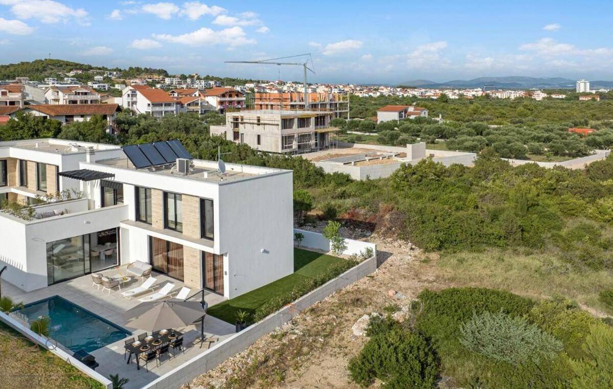 Luftaufnahme einer modernen Villa mit Pool und Solarpaneelen, umgeben von mediterraner Vegetation.
