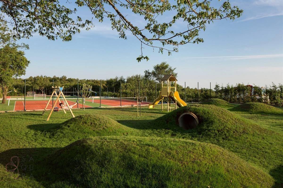Großer Spielplatz mit Rutsche und Schaukeln, umgeben von Grünflächen und Sportanlagen.