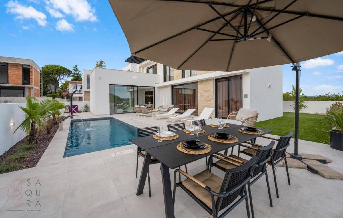 Gemütlicher Essbereich im Freien mit großem Tisch, Sonnenschirm und Blick auf den Pool und Garten.
