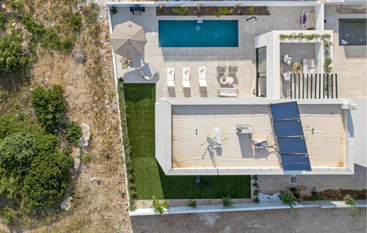 Draufsicht auf eine moderne Villa mit Pool, Sonnenterrasse und Solarpaneelen auf dem Flachdach.