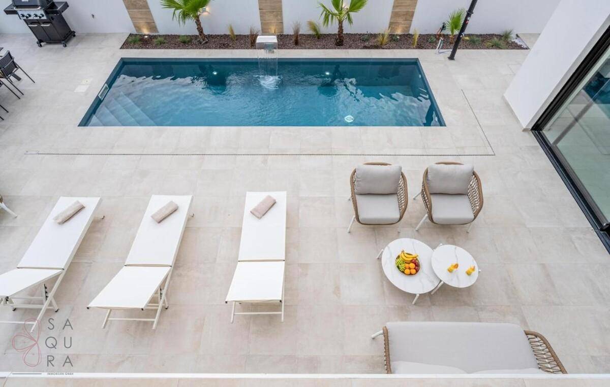 Draufsicht auf den eleganten Poolbereich mit Liegestühlen, Lounge-Möbeln und Wasserspiel.