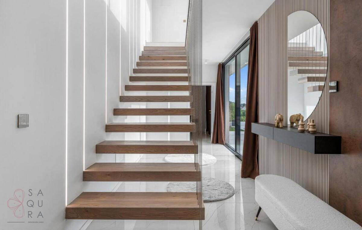 Heller Eingangsbereich mit moderner schwebender Holztreppe und stilvoller Wanddekoration.