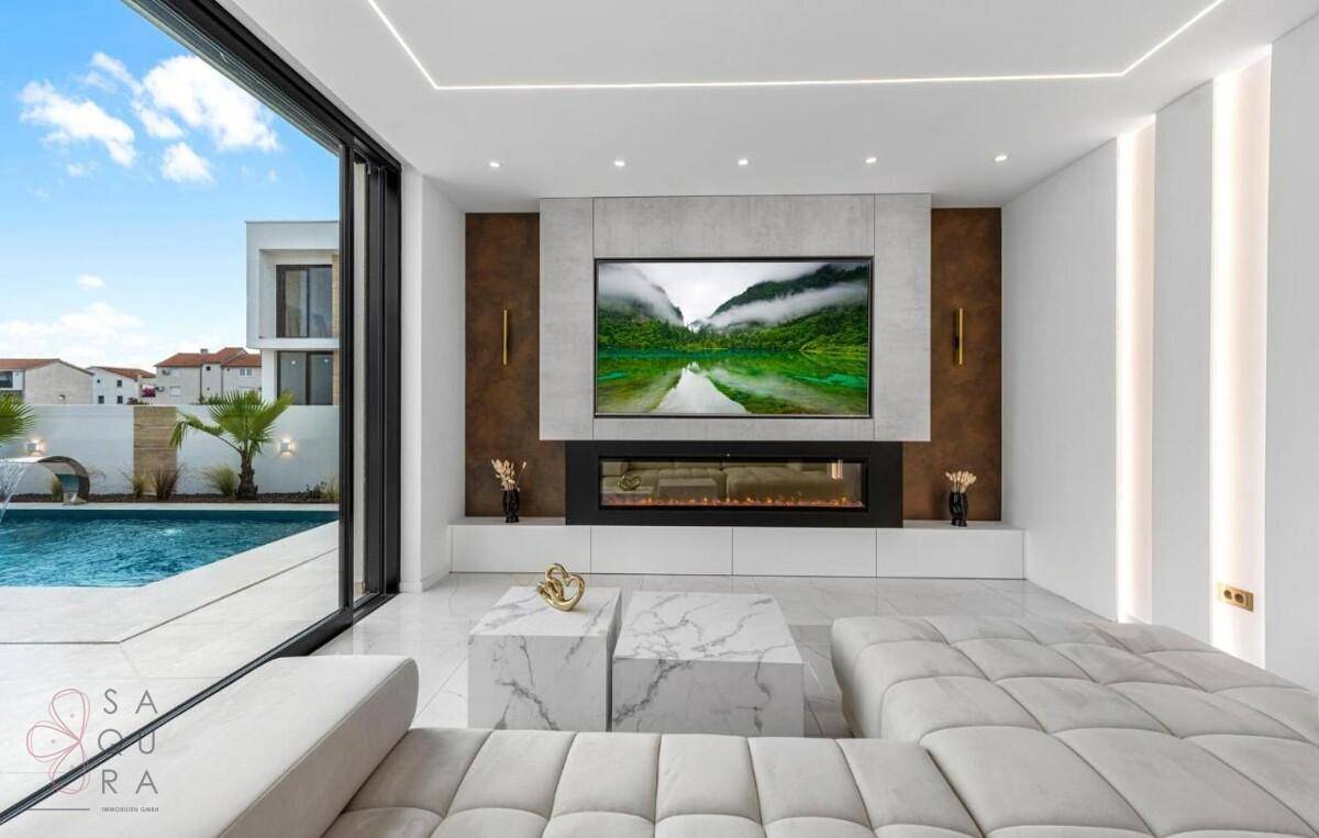 Modernes Wohnzimmer mit großem Fernseher, integriertem Kamin und Blick auf den Pool.