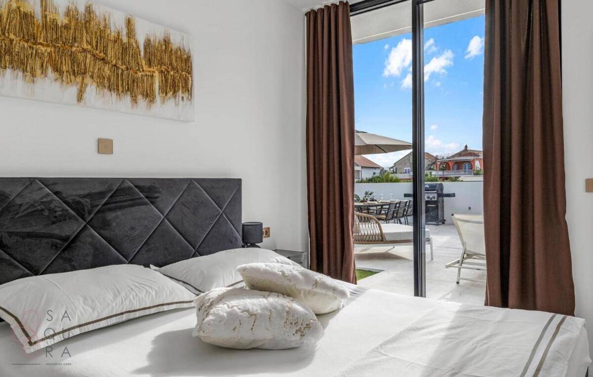 Helles Schlafzimmer mit großem Bett, Kunstwerk und direktem Zugang zur sonnigen Terrasse.