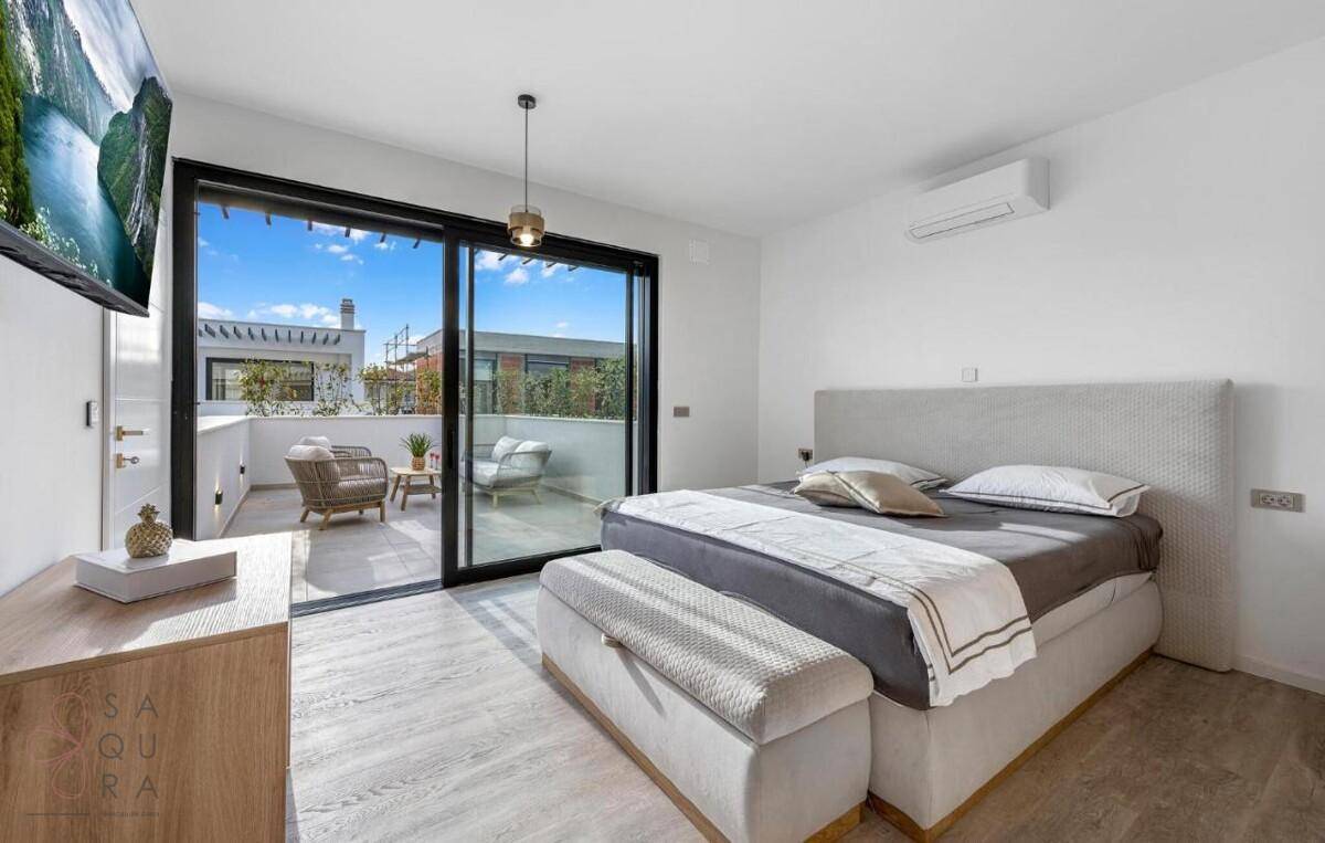 Helles Schlafzimmer mit Balkonzugang, Holzboden und Blick auf die umliegenden Gebäude.