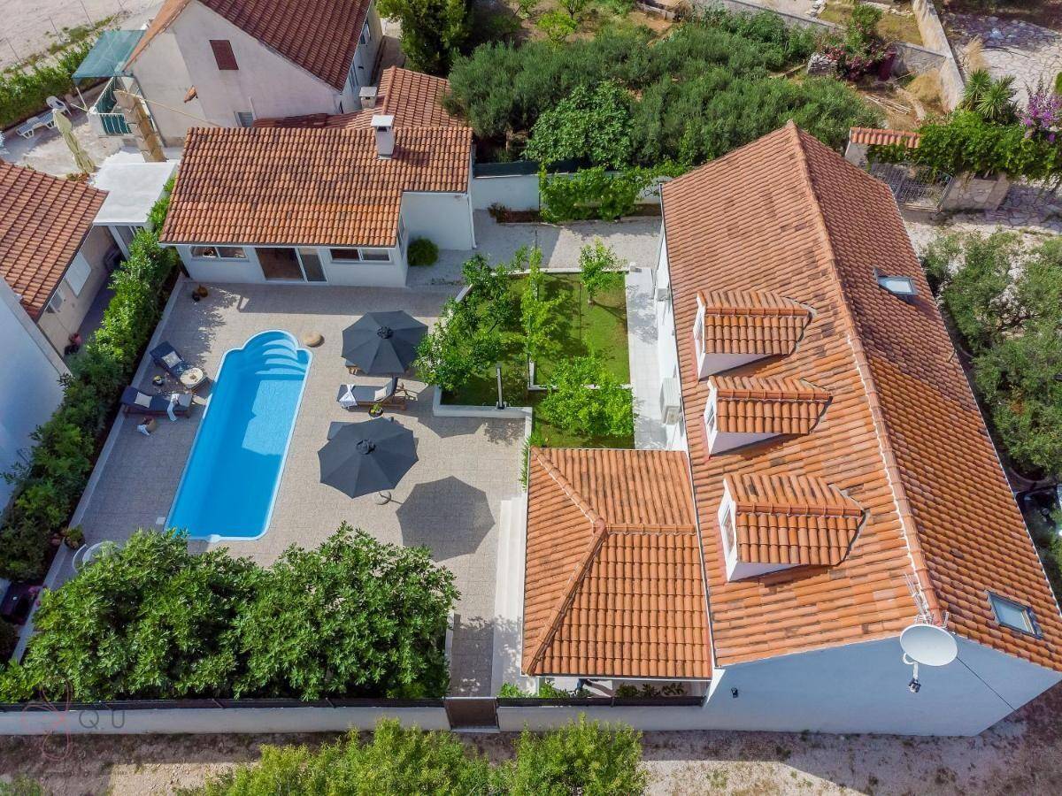 Luftaufnahme des Anwesens mit Pool, Garten und mehreren Gebäuden unter blauem Himmel.
