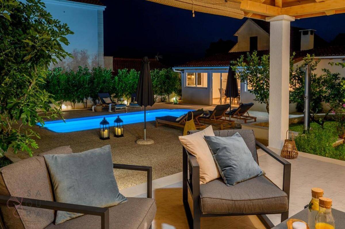 Gemütliche überdachte Terrasse mit bequemen Sitzmöbeln und Blick auf den beleuchteten Pool.