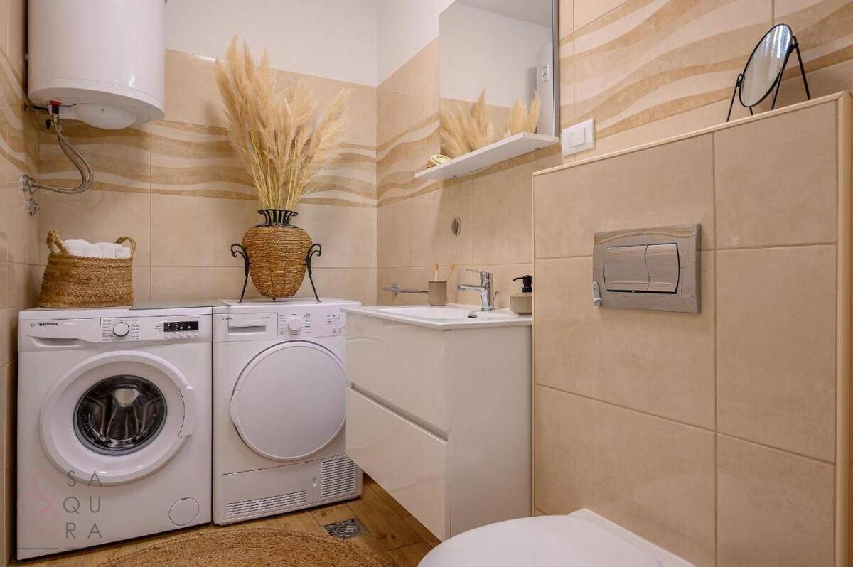 Modernes Badezimmer mit Waschmaschine, Trockner und beigefarbenen Fliesen.